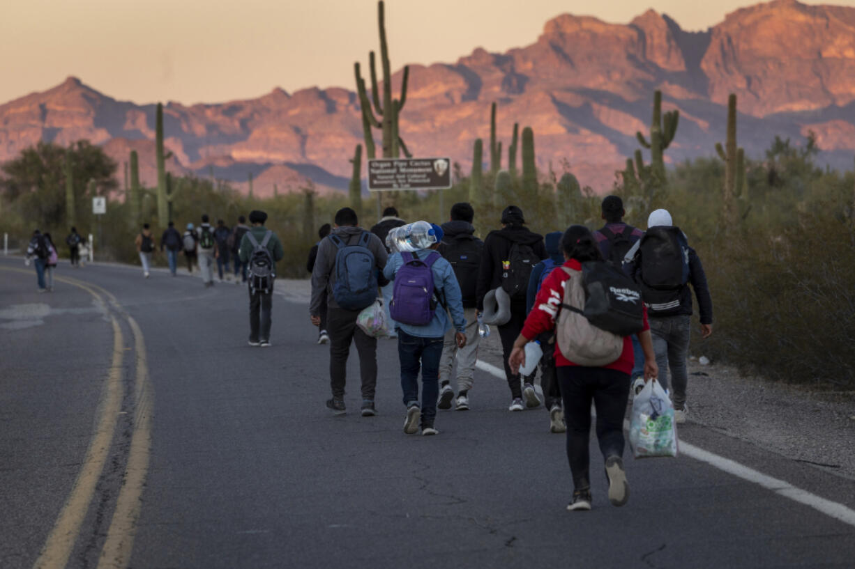 Immigrants walk into the United States after they crossed the U.S.-Mexico border on Dec. 7, 2023, in Lukeville, Arizona. A surge of immigrants illegally passing through openings cut by smugglers into the border wall has overwhelmed U.S. immigration authorities, causing them to shut down several international ports of entry so that officers can help process the new arrivals.