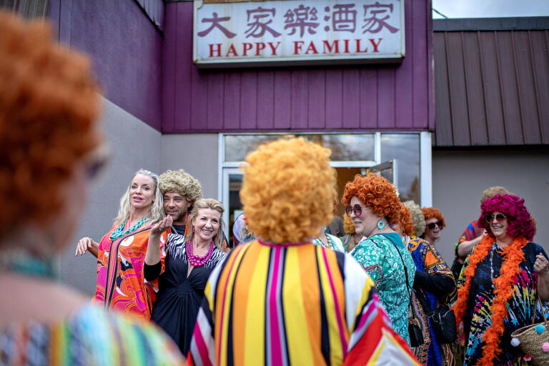 An assortment of smiles, colorful caftans and vibrant wigs are seen outside Happy Family Restaurant in Battle Ground as participants in the Mrs. Roper Pub Crawl gather outside on Saturday evening, March 23, 2024. The restaurant was one of six locations in the downtown area that hosted the pub crawl.