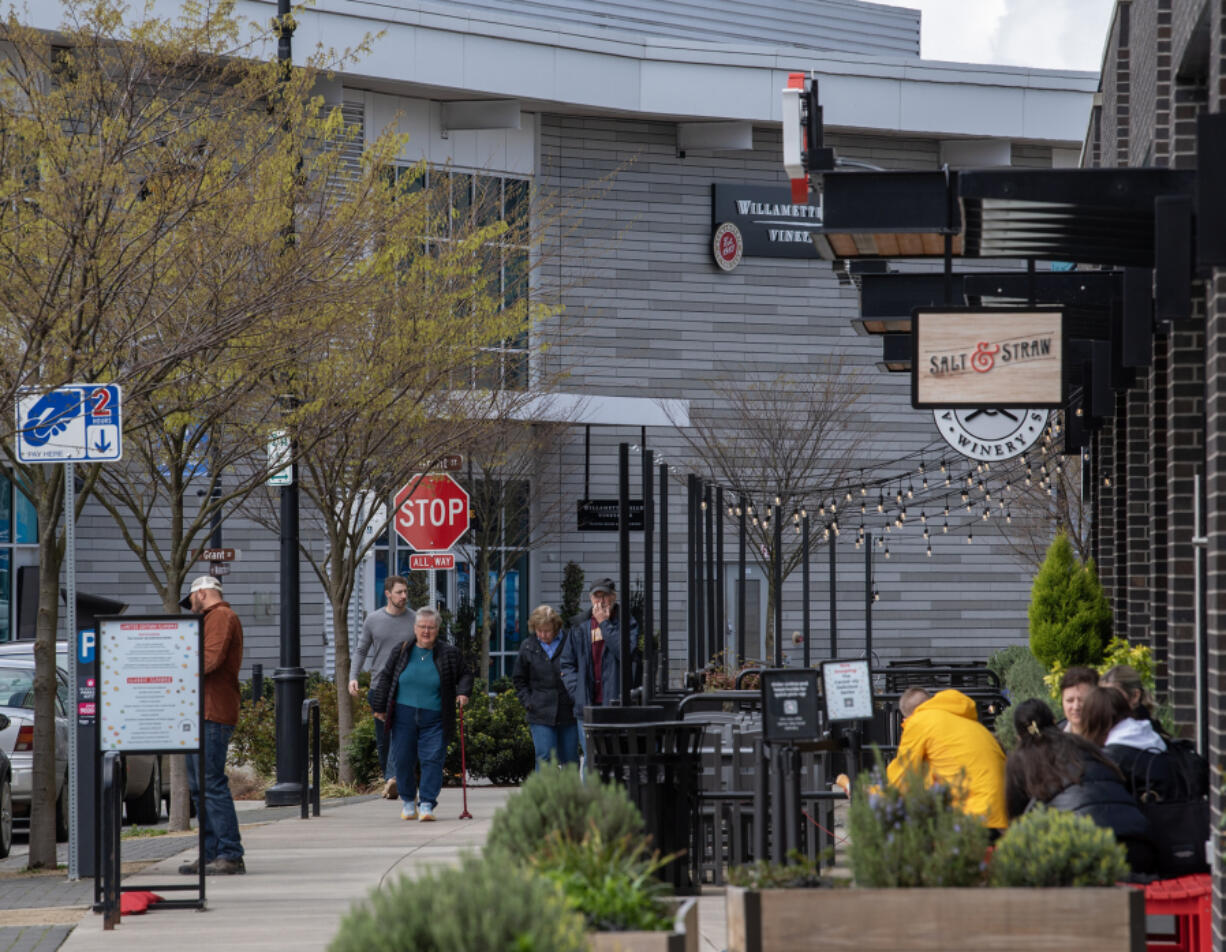 People walk down the sidewalk and sit outside Tuesday at the Waterfront Vancouver. The development along the Columbia River has been a major economic boost for Vancouver over the past few years.