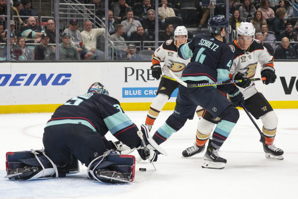 Seattle Kraken goaltender Joey Daccord (35) covers the puck and defenseman Justin Schultz (4) defends as Anaheim Ducks center Ryan Strome (16) moves in during the second period of an NHL hockey game Tuesday, March 26, 2024, in Seattle.