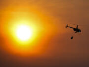 A helicopter carries a bucket as it flies over homes burned by the Smokehouse Creek Fire, Wednesday, Feb. 28, 2024, in Canadian, Texas.