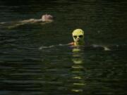 FILE - A woman wearing sun protection headgear and sunglasses swims as residents cool off on a sweltering day at an urban waterway in Beijing, July 10, 2023. Climate change is making heat waves crawl slower across the globe and last longer with higher temperatures over larger areas, a new study finds.