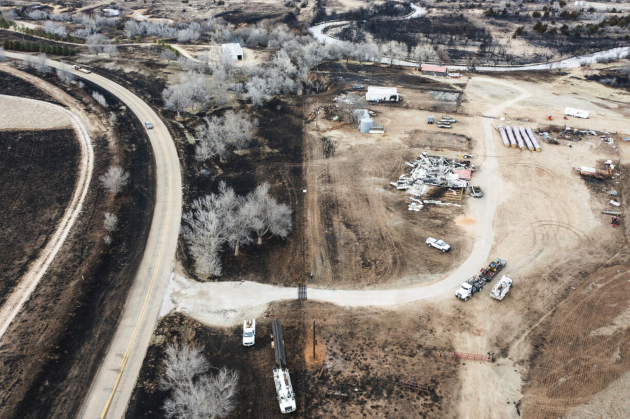 Electrical crews, bottom, replace burnt power poles near a destroyed residence, along the Canadian River in Canadian, Texas, Thursday, Feb. 29, 2024.