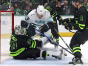 Dallas Stars goaltender Jake Oettinger (29) gets slammed into by Seattle Kraken left wing Brandon Tanev (13) as he shoots in the second period of an NHL hockey game on Saturday, April 13, 2024, in Dallas. (AP Photo/Richard W.