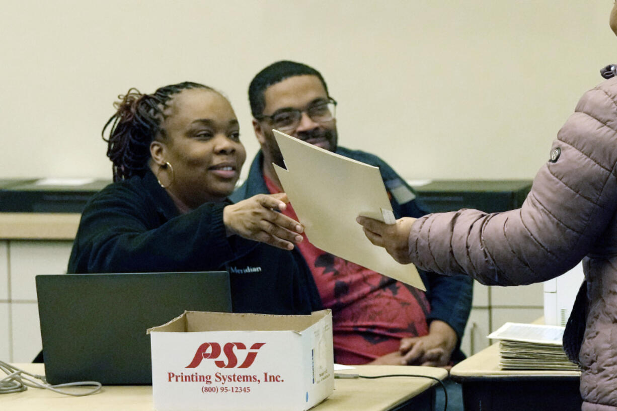 FILE - A ballot is handed to a voter, far right, as early voting takes place at the Warren City Hall, Feb. 21, 2024, in Warren, Mich. The Republican National Committee has filed voting-related lawsuits in two dozen states targeting such things as voter rolls, mailed balloting and policies related to poll watchers. Democrats say it&rsquo;s a strategy designed to raise doubts about the legitimacy of the vote this fall and potentially delay certification of the results.