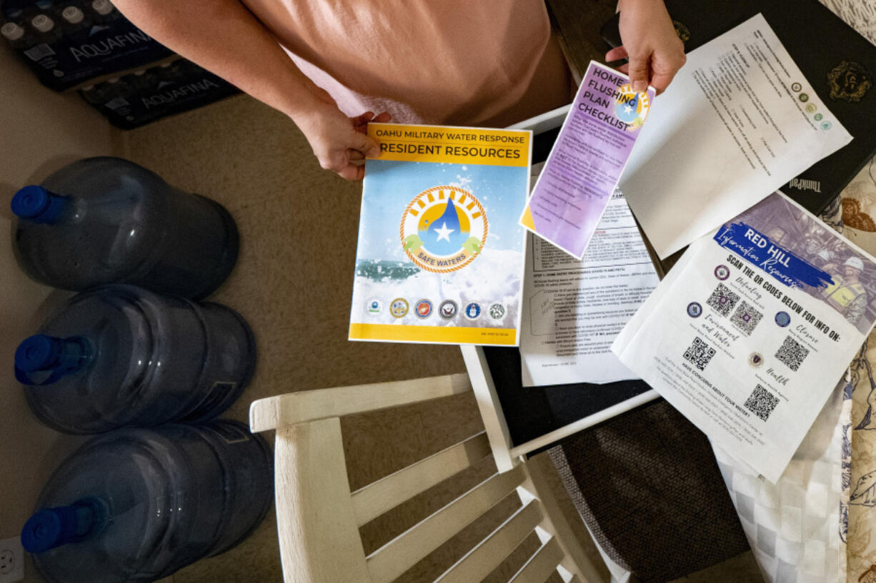 Richelle Dietz holds a couple of brochures containing resources for U.S. military families affected by the on-base housing water contamination from a jet fuel leak in 2021, at her home, Monday, April 22, 2024, in Honolulu, Hawaii.