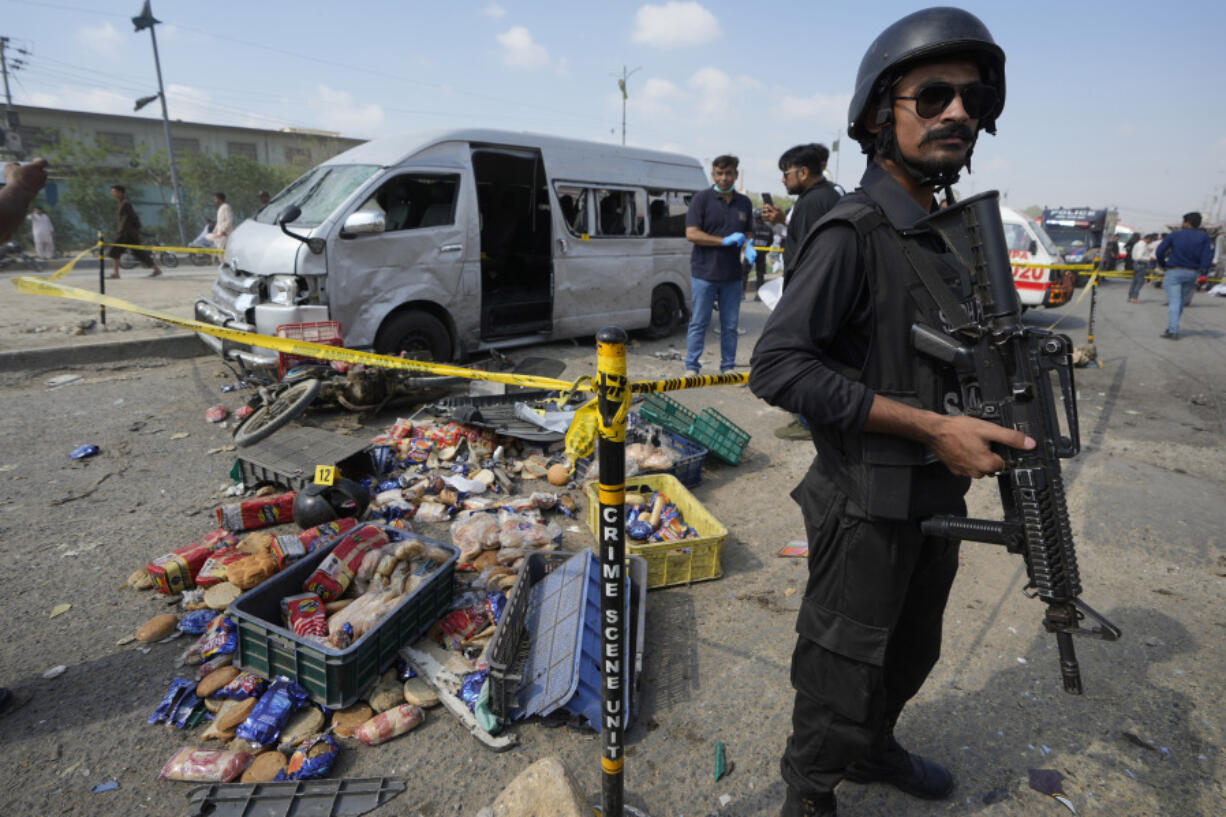 A Pakistani police officer stands guard as investigators examine the site of a suicide attack in Karachi, Pakistan, Friday, April 19, 2024.