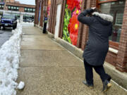 A woman walks past a photographic mural depicting colorful flowers in Concord, N.H., Friday, April 5, 2024, a day after a Spring storm dumped snow across the region.