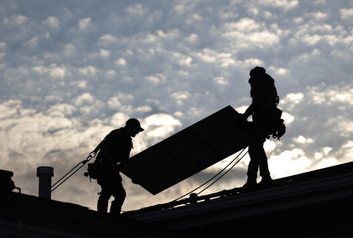 Jared Salvatore, left, and Garrison Riegel, of Celestar Solar, carry a solar panel onto a roof Nov. 30 in Schaumburg, Ill.