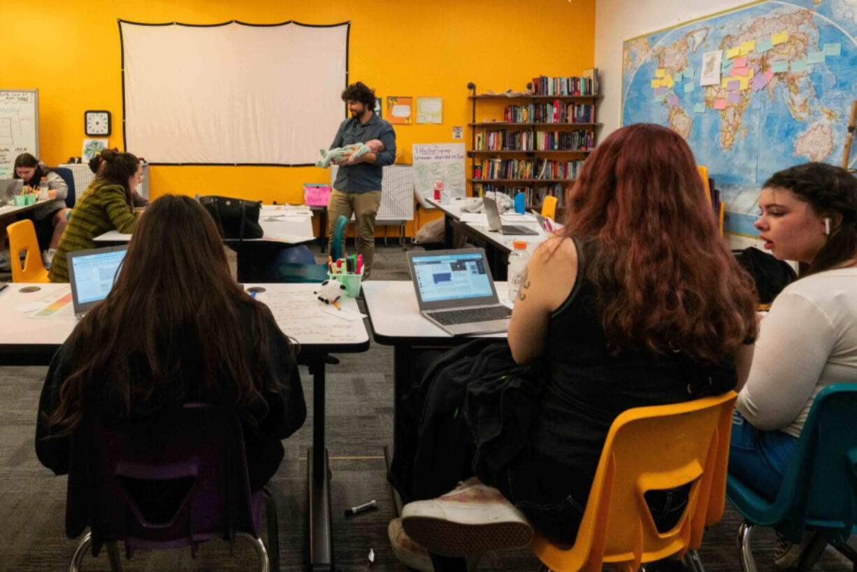 History teacher Trevor Bradley holds a student&rsquo;s baby while his class completes coursework at Lumen High School in Spokane.