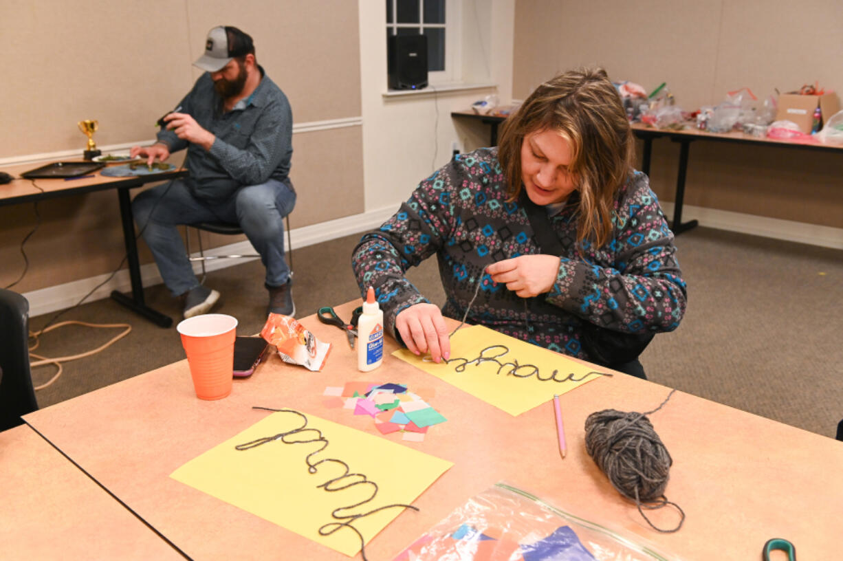 Angie Vis, right, strings together her project while Josh Plunkett, left, uses the hot glue gun at the Camas Public Library&rsquo;s Feb. 17 Bad Art Night.
