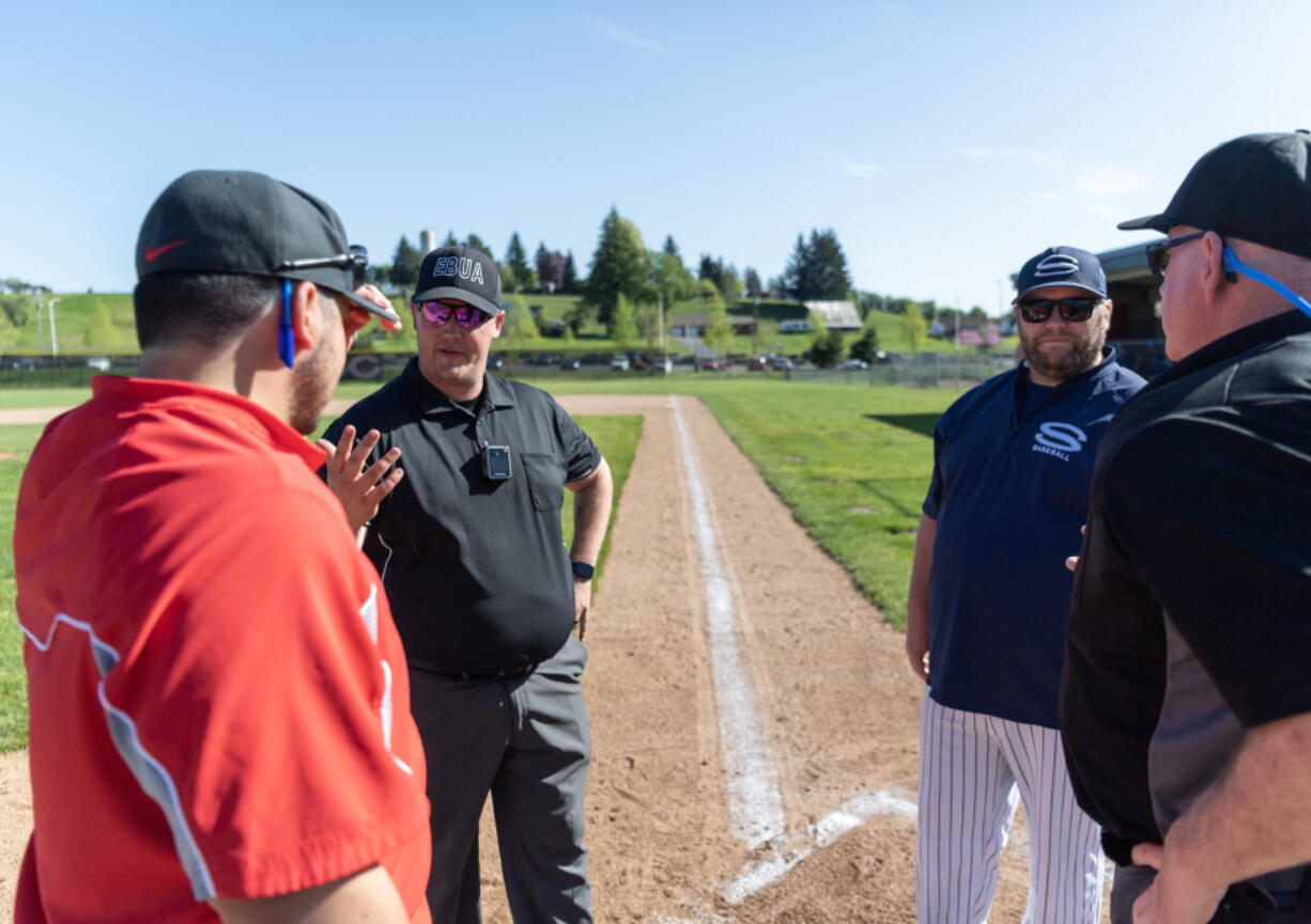 Umpire John Telyea, second from left, talks with Camas JV coach Liam Fitzpatrick, left, Skyview JV coach Trevor Mueller, second from right, and umpire Fritz Porter on April 23 at Camas High School. Telyea is one of a handful of baseball and softball high school umpires in Clark County wearing body cameras as part of a Washington Interscholastic Activities Association pilot program.