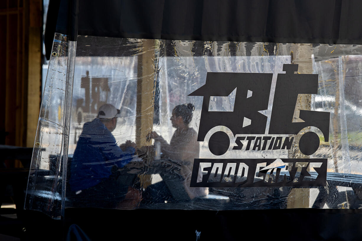 Arthur Colunga of Battle Ground, left, and his wife, Lyndsey, grab a bite to eat Thursday while enjoying the outdoor seating area at the new Battle Ground Station food cart pod on Main Street. At top, a customer picks up an order from Bobablastic in Battle Ground on Thursday morning.