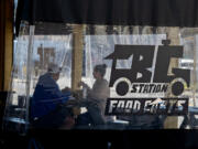 Arthur Colunga of Battle Ground, left, and his wife, Lyndsey, grab a bite to eat Thursday while enjoying the outdoor seating area at the new Battle Ground Station food cart pod on Main Street. At top, a customer picks up an order from Bobablastic in Battle Ground on Thursday morning.