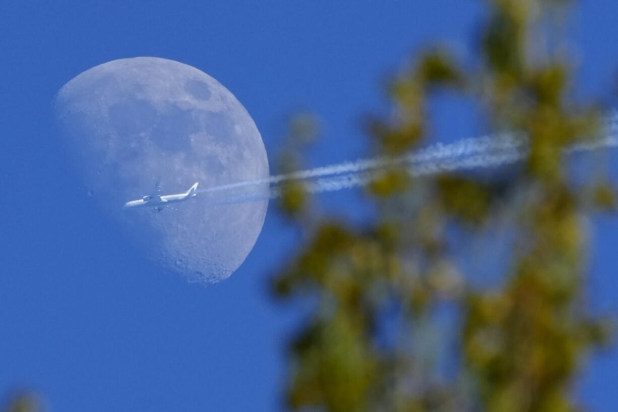 A Boeing 787-9 Dreamliner jet belonging to Air China, flying from Madrid to Beijing, passes the moon Friday over the village of Podolye, 43 miles east of St. Petersburg, Russia.