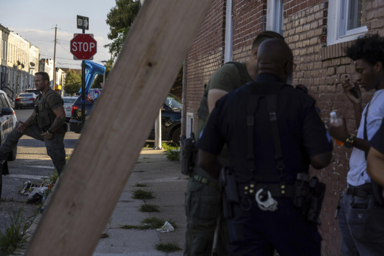 Police officers question a boy during a vigil for Antonio Lee, Friday, Aug. 18, 2023, in Baltimore. Lee, 19, was shot and killed while squeegeeing in Baltimore.