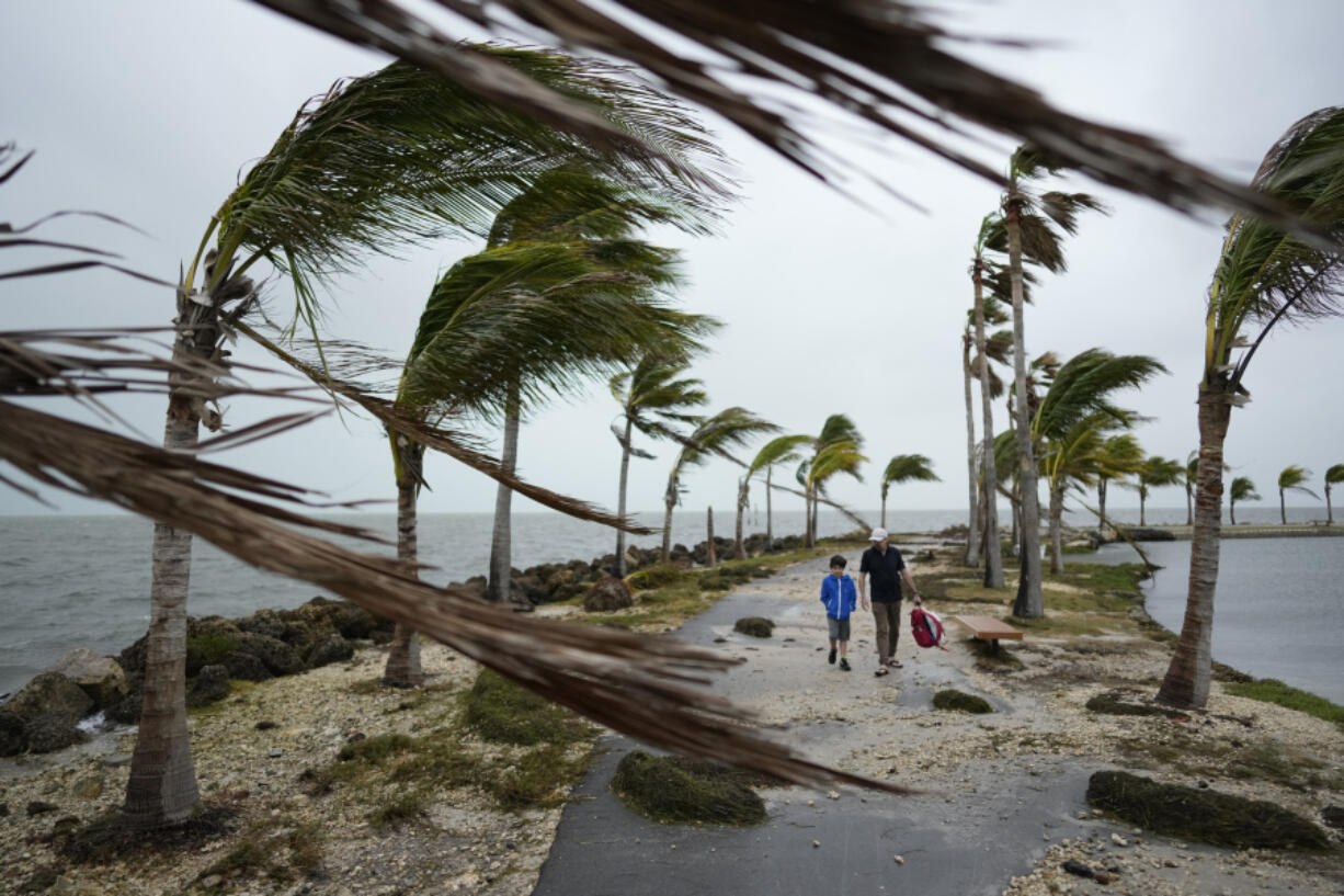 FILE - Bob Givehchi, right, and his son Daniel, 8, Toronto residents visiting Miami for the first time, walk past debris and palm trees blowing in gusty winds, at Matheson Hammock Park in Coral Gables, Fla., Dec. 15, 2023. Nearly all the experts think 2024 will be one of the busiest Atlantic hurricane seasons on record.