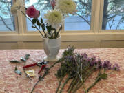 A supermarket bouquet of three white chrysanthemums, a lily stem and a single rose in a decorative pitcher, along with garden pruners and a packet of flower-preserving granules.