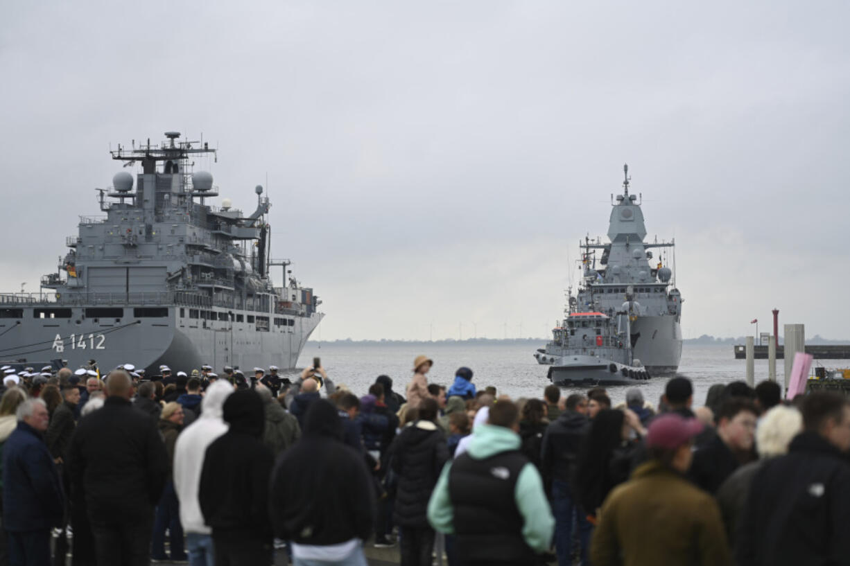 People gather as they watch the frigate &ldquo;Hessen&rdquo;, right, arriving  in the harbour in Wilhelmshaven, Germany, Sunday May 5, 2024. The frigate &ldquo;Hessen&rdquo; returned to Wilhelmshaven after taking part in the European Union mission to help defend cargo ships from Houthi attacks in the Red Sea.