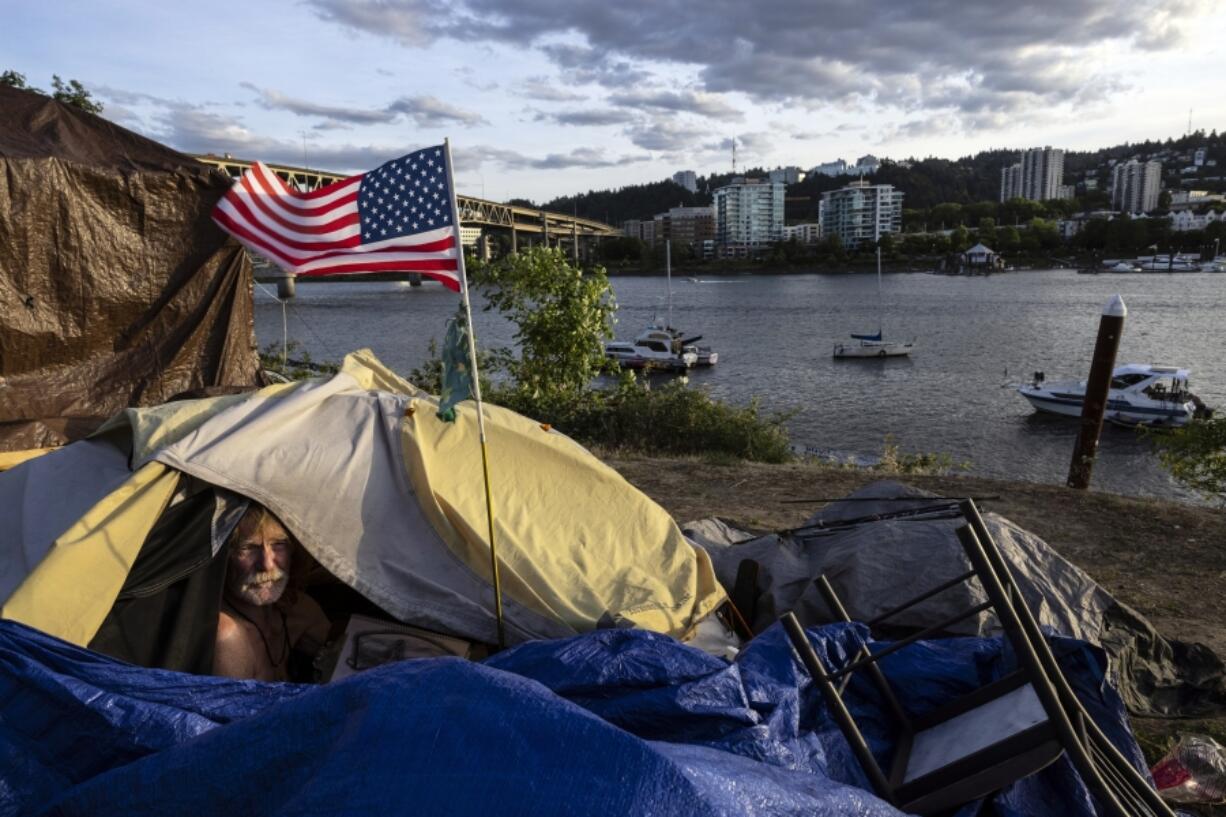 FILE - Frank, a homeless man sits in his tent with a river view in Portland, Ore., Saturday, June 5, 2021. The city council in Portland, Oregon, has approved new homeless camping rules. Under the rules, people who reject offers of shelter can face penalties, including fines of up to $100 or up to seven days in jail.