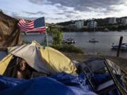 FILE - Frank, a homeless man sits in his tent with a river view in Portland, Ore., Saturday, June 5, 2021. The city council in Portland, Oregon, has approved new homeless camping rules. Under the rules, people who reject offers of shelter can face penalties, including fines of up to $100 or up to seven days in jail.