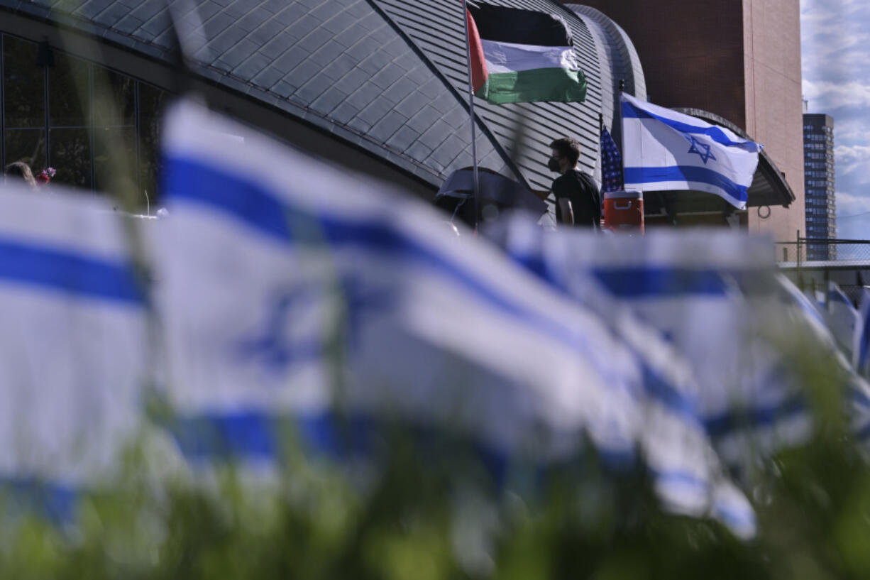 A man walks below flags flyng at a Pro-Palestinian encampment at MIT, Thursday, May 9, 2024, in Cambridge, Mass. MIT has suspended 23 students for participating in the encampment, and police detained at least three during a demonstration at the nearby Stata center, where demonstrators blocked traffic over claims the university was conducting research which would be used for Israeli military drones.