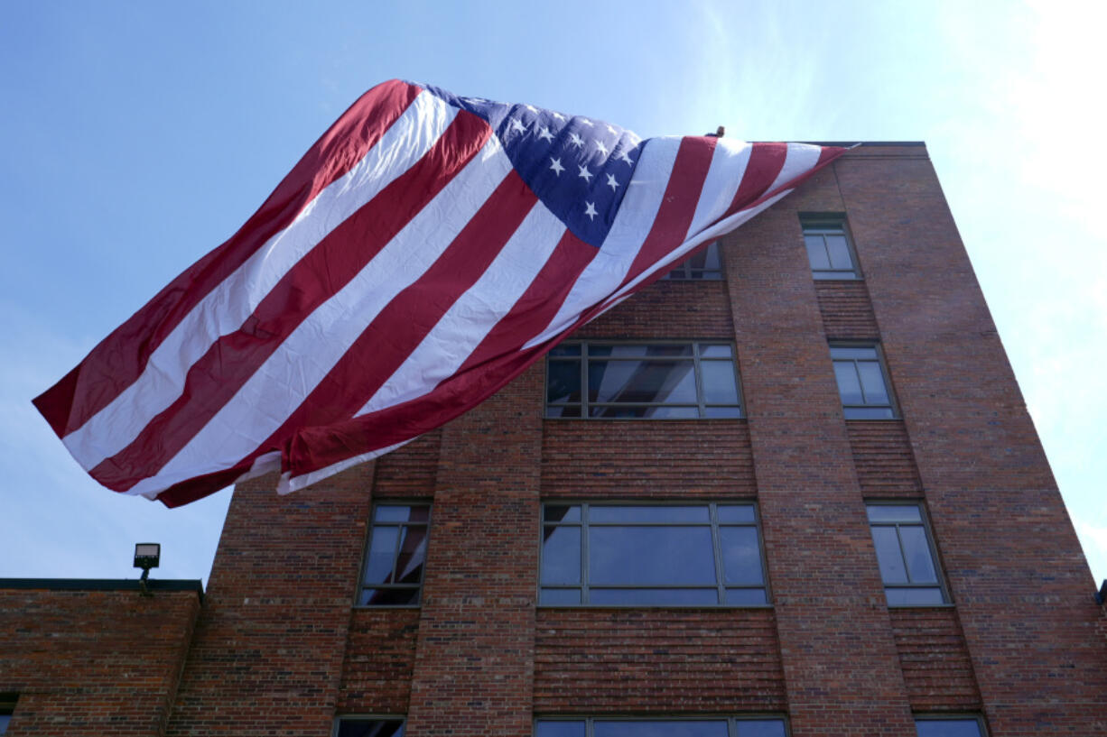A giant American flag is unfurled on Lisner Hall on the campus of George Washington University in Washington, Friday, May 3, 2024, as demonstrators protest the Israel-Hamas war.
