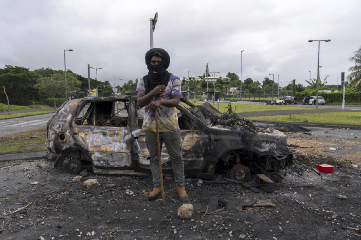 A man stands in front a burnt car after unrest in Noumea, New Caledonia, Wednesday May 15, 2024. France has imposed a state of emergency in the French Pacific territory of New Caledonia. The measures imposed on Wednesday for at least 12 days boost security forces&rsquo; powers to quell deadly unrest that has left four people dead, erupting after protests over voting reforms.