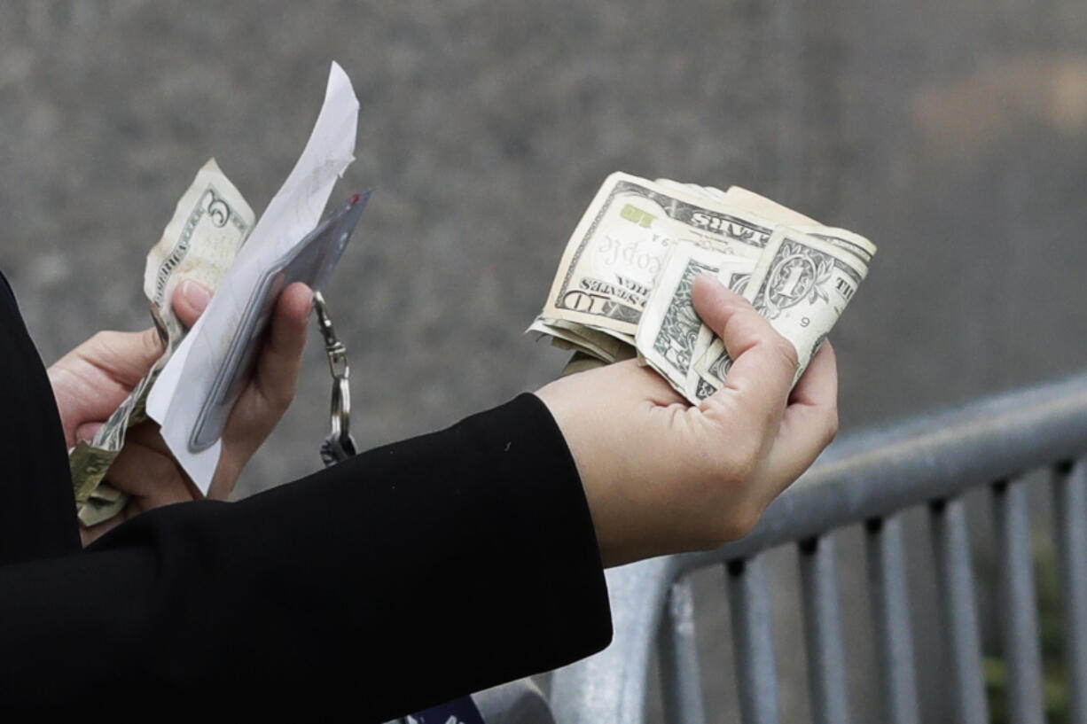 A woman pays with cash as she buys from a street vendor, Sept. 26, 2017 in New York. Despite numbers showing a healthy economy overall, lower-income spenders are showing the strain.