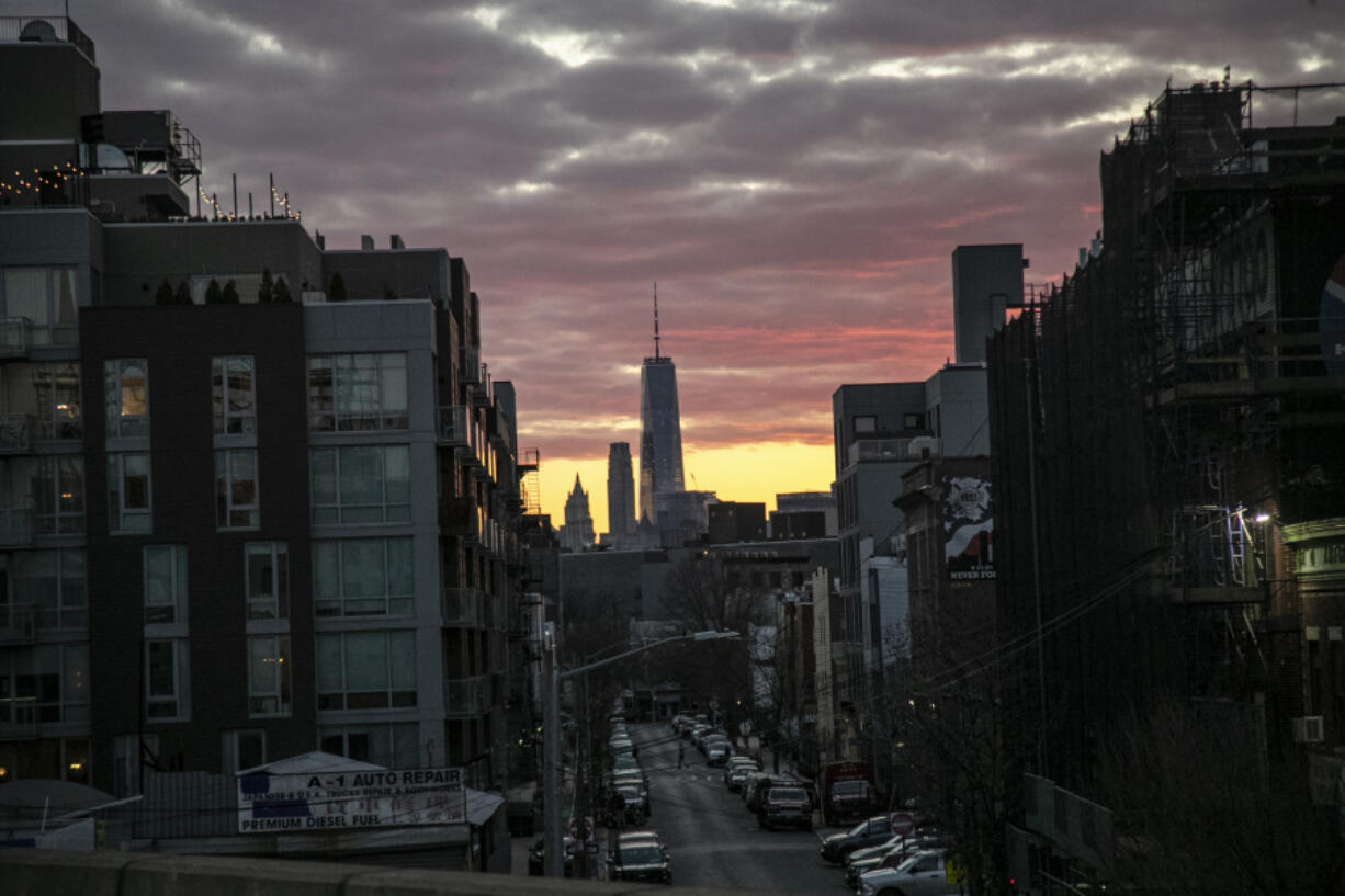 FILE - A man crosses a street against the backdrop of One World Trade Center at dusk in New York, on Saturday, March 21, 2020.