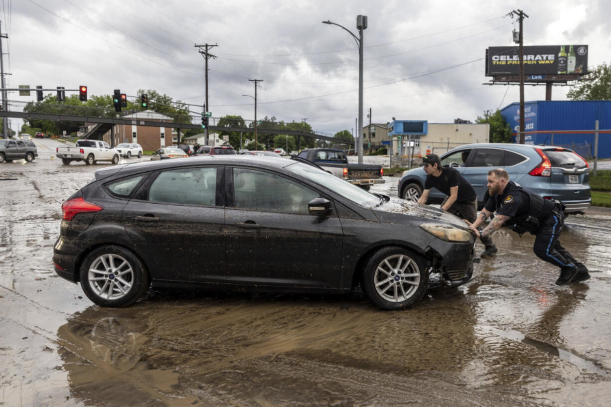 A police officer and an employee of nearby Dingman&#039;s Collision Center push a car that had been caught in flood waters in Omaha, Neb.