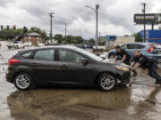 A police officer and an employee of nearby Dingman&#039;s Collision Center push a car that had been caught in flood waters in Omaha, Neb.