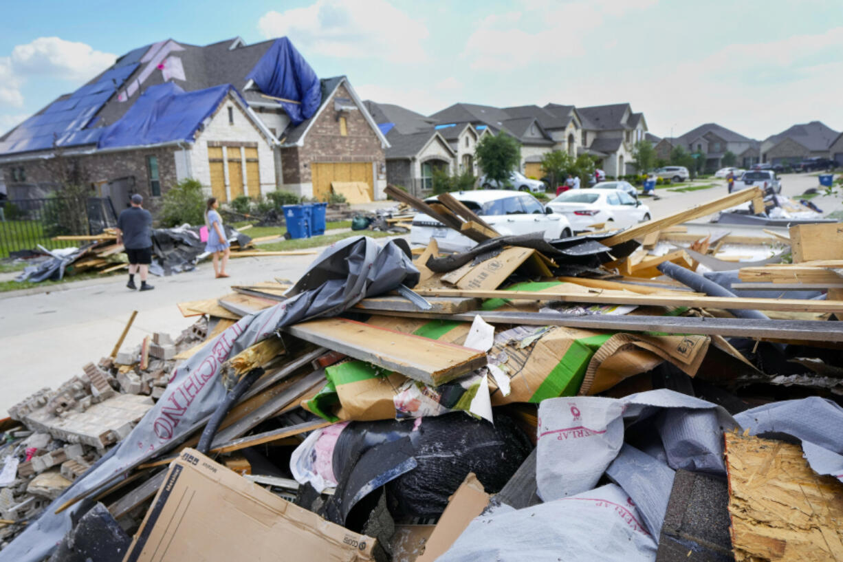 People walk through a Bridgeland neighborhood as families begin cleaning up storm damage, Sunday, May 19, 2024, in Cypress, Texas.