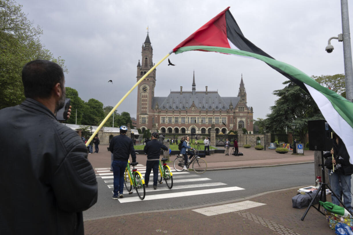 A lone demonstrator waves the Palestinian flag outside the Peace Palace, rear, housing the International Court of Justice, or World Court, in The Hague, Netherlands, Friday, May 24, 2024. The top United Nations court was to rule on an urgent plea by South Africa for judges to order Israel to halt its military operations in Gaza and withdraw from the enclave.
