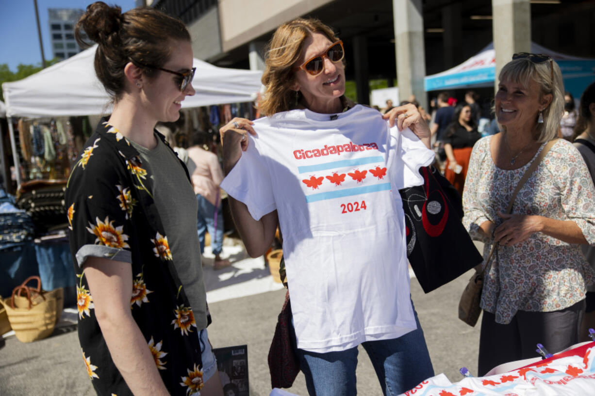 Mary Beth McCarthy, center, holds a Cicadapalooza shirt sold by Trayce Zimmermann at her self-described &ldquo;cicada chic&rdquo; apparel booth on May 25, at the Randolph Street Market in Chicago.