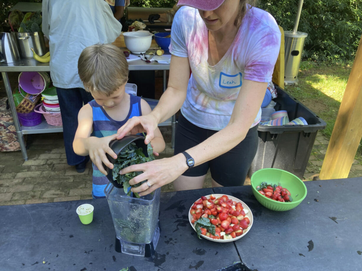 Grow It organizer Leah Reichardt-Osterkatz, right, helps children make smoothies from strawberries they picked, plus kale grown on the farm May 29 at Spring Forest in Hillsborough, N.C.