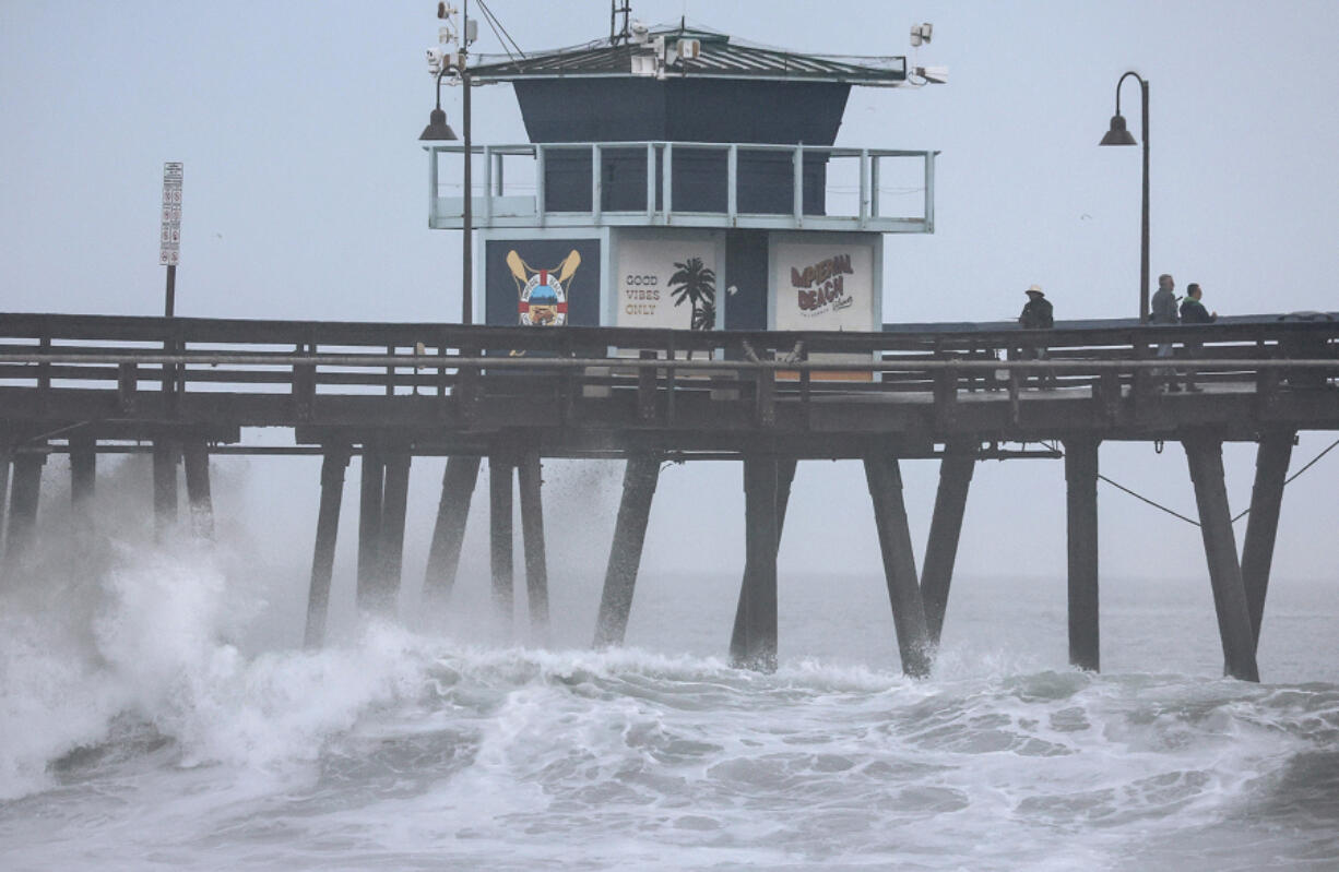 People stand on a pier over the Pacific Ocean with Tropical Storm Hilary approaching in San Diego County on Aug. 20, 2023, in Imperial Beach, California.