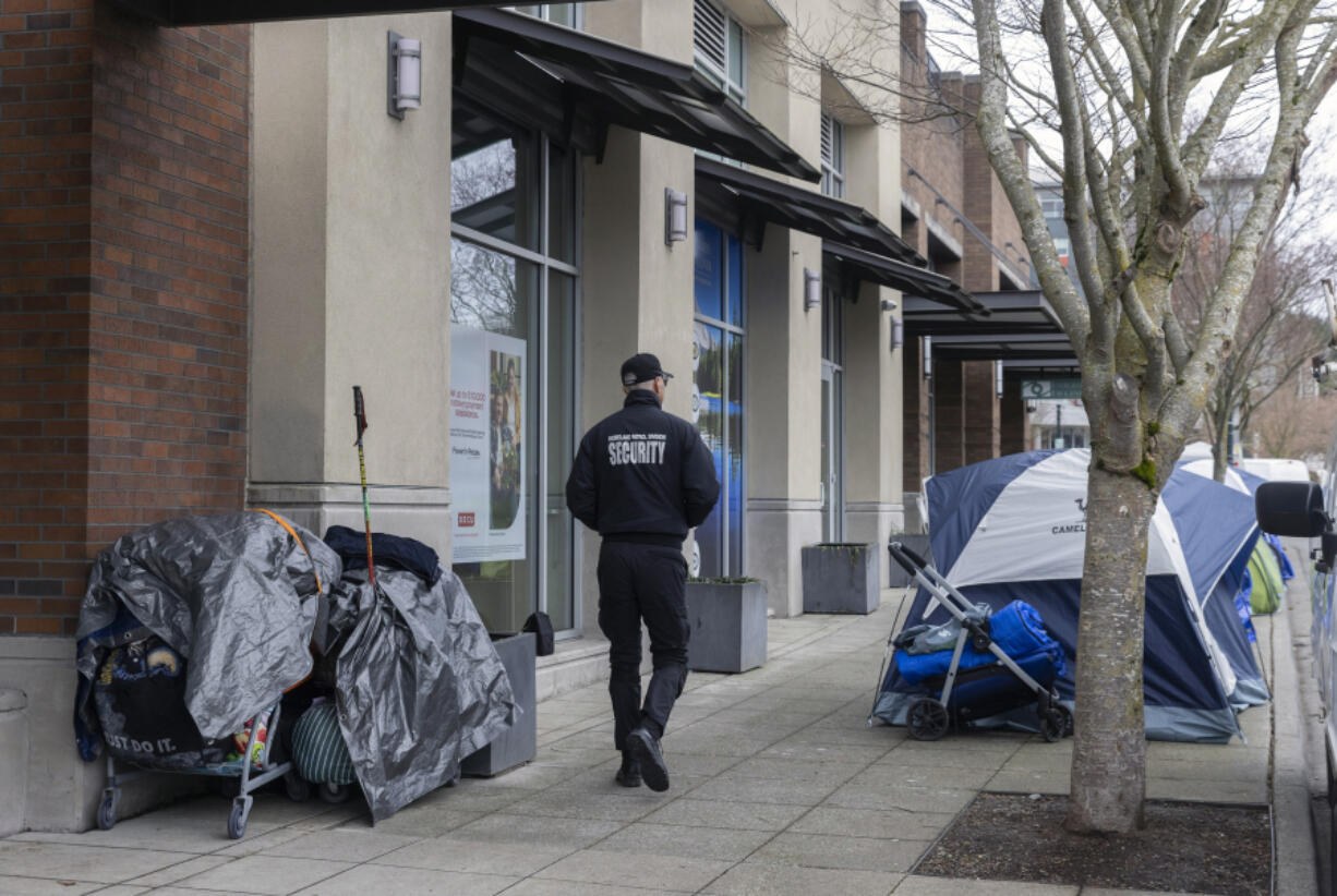 A security guard from Burien City Hall walks past tents along Fifth Avenue Southwest and Southwest 152nd Street, March 11, 2024, in Burien, Wash. (Ellen M.