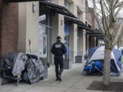 A security guard from Burien City Hall walks past tents along Fifth Avenue Southwest and Southwest 152nd Street, March 11, 2024, in Burien, Wash. (Ellen M.