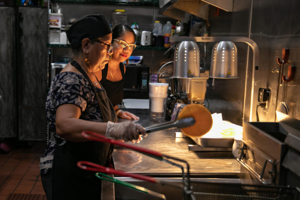 Zacil Vazquez, right, helps her mother Maria Vazquez prepare an order for a customer at their restaurant Sazon in Huntington Park, California, on Sept. 9, 2022. Just weeks before the July 1, 2024, start of a statewide ban on so-called &ldquo;hidden fees,&rdquo; state Sen. Bill Dodd, a Democrat, has proposed a new law to clarify how it applies to the restaurant industry.