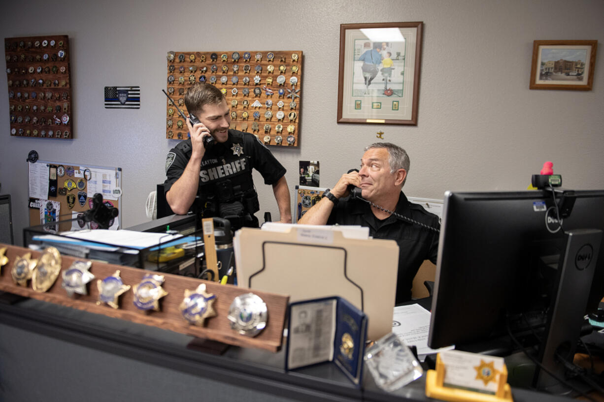 Deputy Bryson Layton, left, of the Clark County Sheriff's Office jokingly talks on his radio as he mimics his dad, Deputy DuWayne Layton, taking a call at his desk June 3 in downtown Vancouver. DuWayne Layton said his son was like his shadow when the 22-year-old was a boy, and they now work together at the sheriff&rsquo;s office.