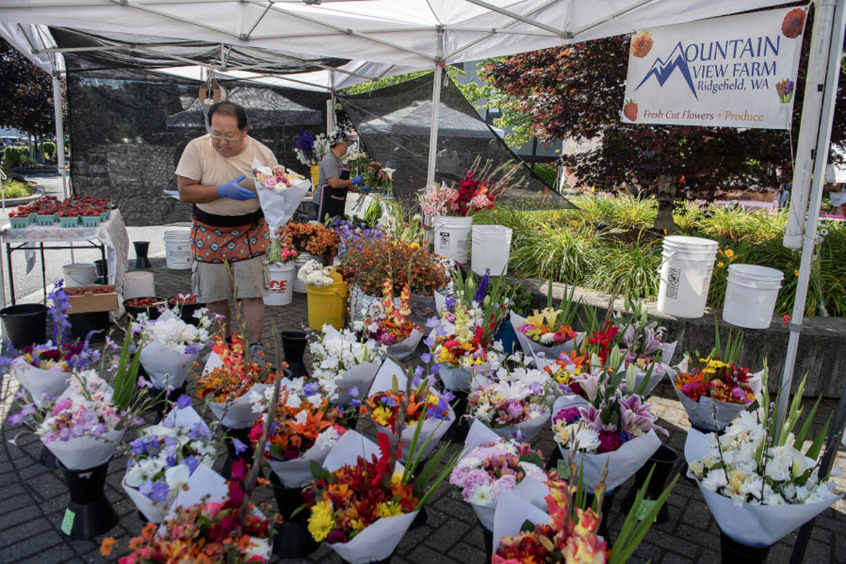 Thai Lee, left, and wife Bao Vang of Mountain View Farm display bouquets of colorful flowers for customers at the East Vancouver Farmers Market on Thursday morning.