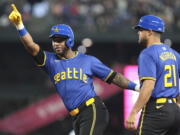 Seattle Mariners' Victor Robles, left, celebrates next to first base coach Kristopher Negrón (21) after getting a hit off Texas Rangers pitcher Andrew Heaney during the first inning of a baseball game, Friday, June 14, 2024, in Seattle.