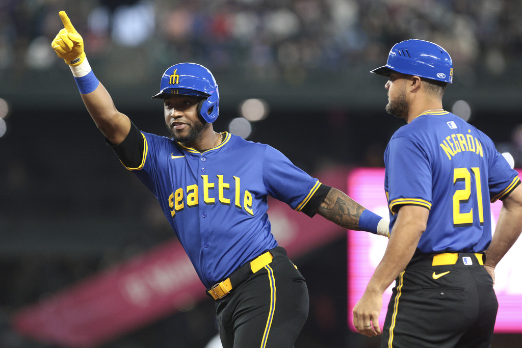 Seattle Mariners' Victor Robles, left, celebrates next to first base coach Kristopher Negrón (21) after getting a hit off Texas Rangers pitcher Andrew Heaney during the first inning of a baseball game, Friday, June 14, 2024, in Seattle.