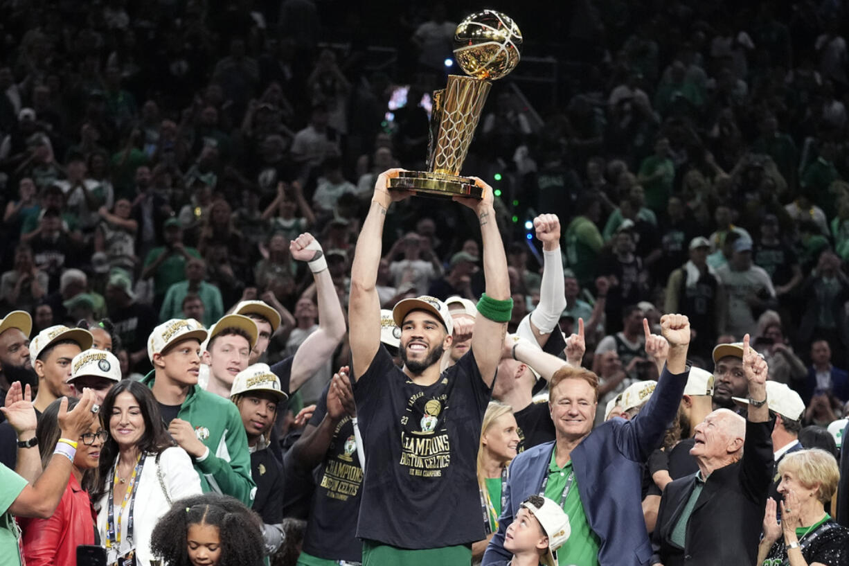 Boston Celtics forward Jayson Tatum holds, center, up the Larry O'Brien Championship Trophy as he celebrates with the team after they won the NBA basketball championship with a Game 5 victory over the Dallas Mavericks, Monday, June 17, 2024, in Boston.