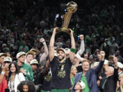 Boston Celtics forward Jayson Tatum holds, center, up the Larry O'Brien Championship Trophy as he celebrates with the team after they won the NBA basketball championship with a Game 5 victory over the Dallas Mavericks, Monday, June 17, 2024, in Boston.