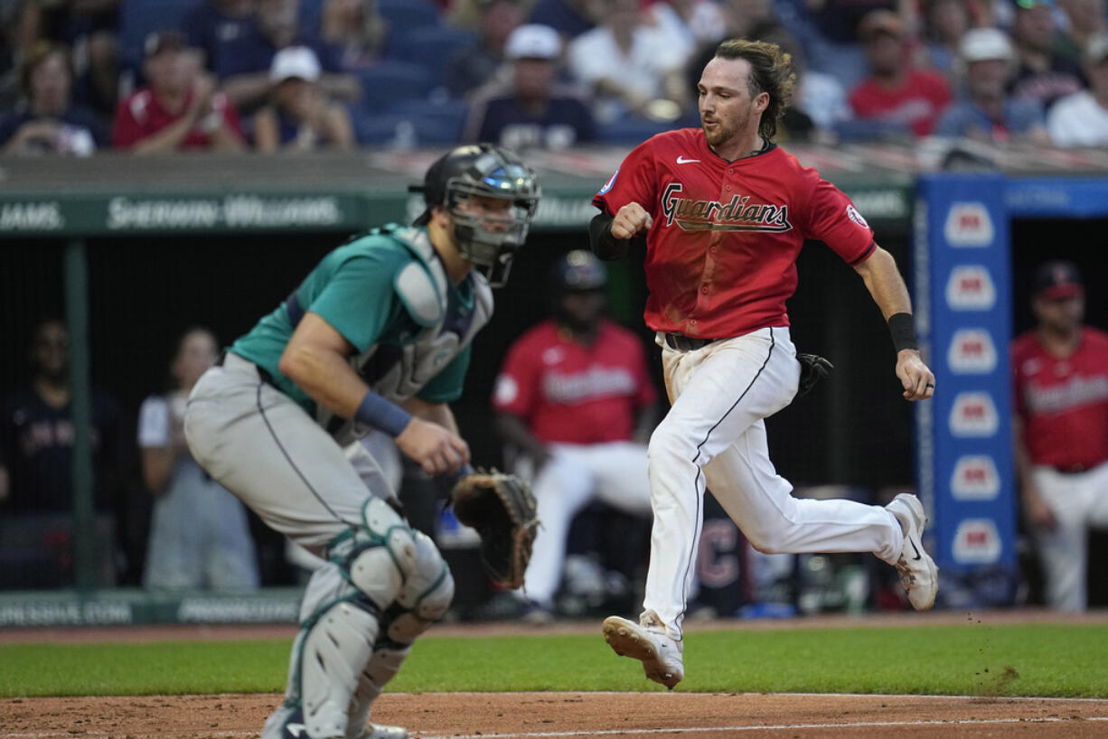 Cleveland Guardians' Daniel Schneemann, runs past Seattle Mariners catcher Cal Raleigh to score during the sixth inning of a baseball game Wednesday, June 19, 2024, in Cleveland.