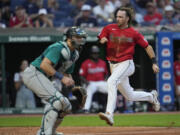 Cleveland Guardians' Daniel Schneemann, runs past Seattle Mariners catcher Cal Raleigh to score during the sixth inning of a baseball game Wednesday, June 19, 2024, in Cleveland.