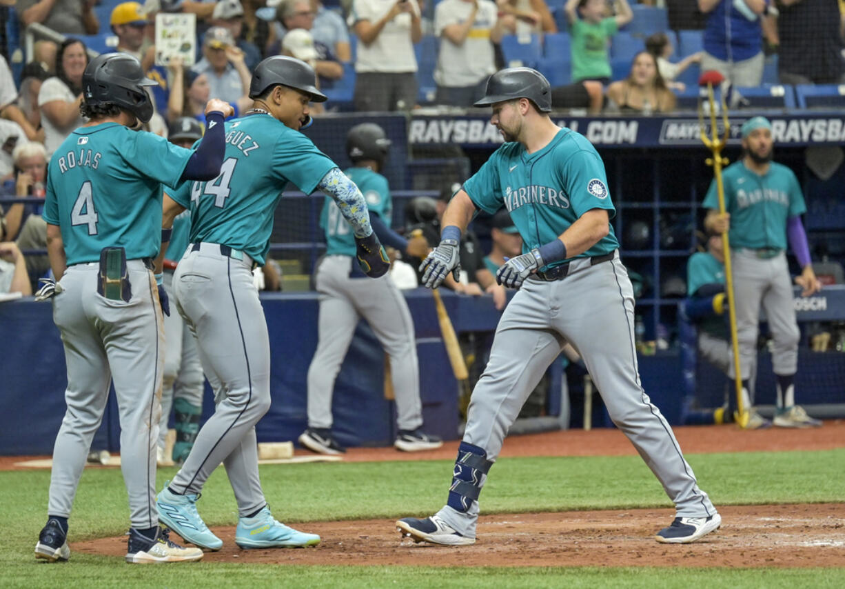 Seattle Mariners third baseman Josh Rojas (4) and Julio Rodríguez (44) congratulate Cal Raleigh after scoring on Raleigh's three-run home run off Tampa Bay Rays reliever Shawn Armstrong during the sixth inning of a baseball game Wednesday, June 26, 2024, in St. Petersburg, Fla.