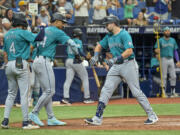 Seattle Mariners third baseman Josh Rojas (4) and Julio Rodríguez (44) congratulate Cal Raleigh after scoring on Raleigh's three-run home run off Tampa Bay Rays reliever Shawn Armstrong during the sixth inning of a baseball game Wednesday, June 26, 2024, in St. Petersburg, Fla.